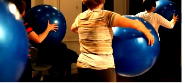Trzy kobiety widoczne od tyłu, trzymają duże niebieskie piłki do ćwiczeń.