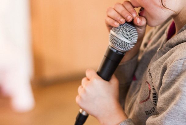 Zbliżenie na mikrofon trzymany w ręku przez dziewczynkę.